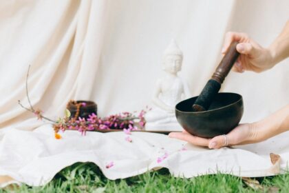 Hands holding a Tibetan singing bowl for meditation in a serene setting with a Buddha figurine and flowers.