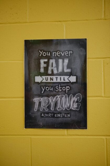 A poster on a yellow wall reading "You never fail until you stop trying"